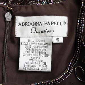May include: A brown silk dress with beaded embellishments. The label reads "Adrianna Papell Occasions" and indicates the dress is size 6, made of 100% silk, and lined with 100% polyester.