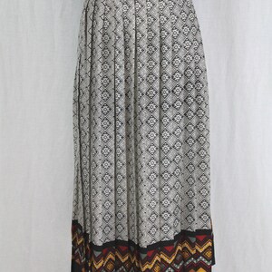 May include: A black and white pleated skirt with a geometric pattern. The skirt has a black waistband with a gold buckle and a colorful geometric border at the hem.
