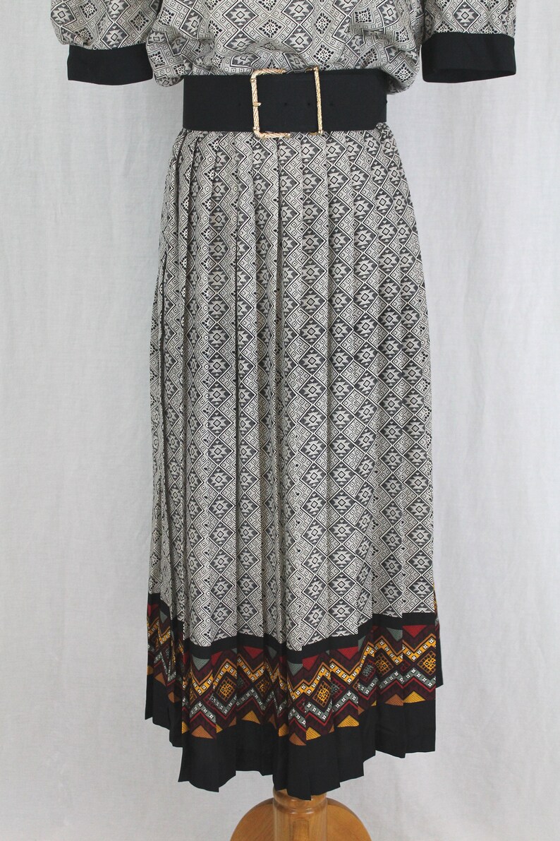 May include: A black and white pleated skirt with a geometric pattern. The skirt has a black waistband with a gold buckle and a colorful geometric border at the hem.