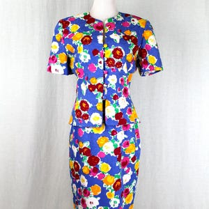 May include: A blue floral print skirt suit with a short-sleeved jacket and a pencil skirt. The suit features a bright floral pattern with pink, yellow, red, and white flowers on a blue background.