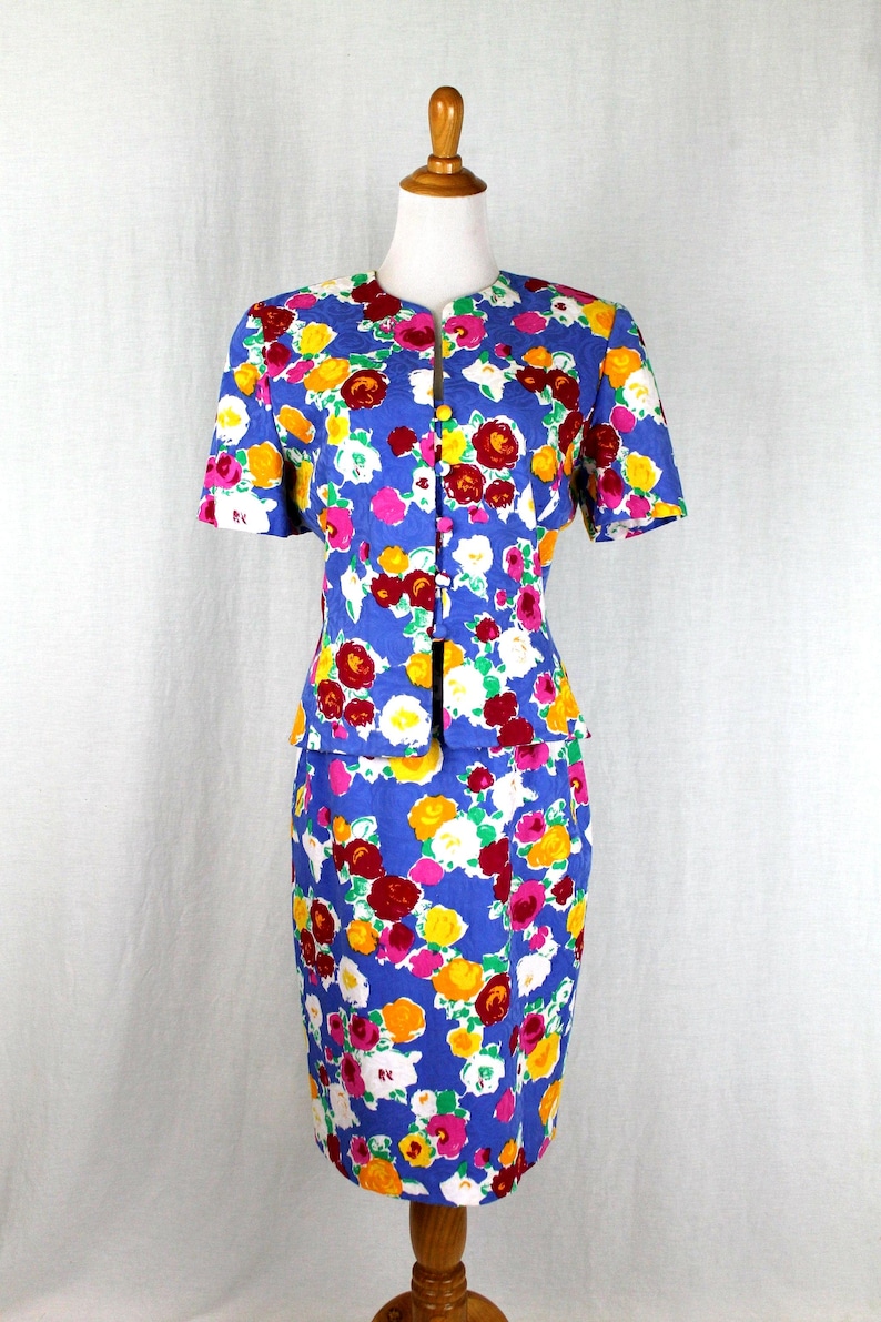 May include: A blue floral print skirt suit with a short-sleeved jacket and a pencil skirt. The suit features a bright floral pattern with pink, yellow, red, and white flowers on a blue background.