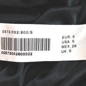 May include: A white tag with black text and a barcode. The tag shows the size of the garment in different sizing systems: EUR. S, USA. S, MEX. 26, UK. S. The tag also includes the product number 0573/052/800/S and the barcode number 00573052800022.