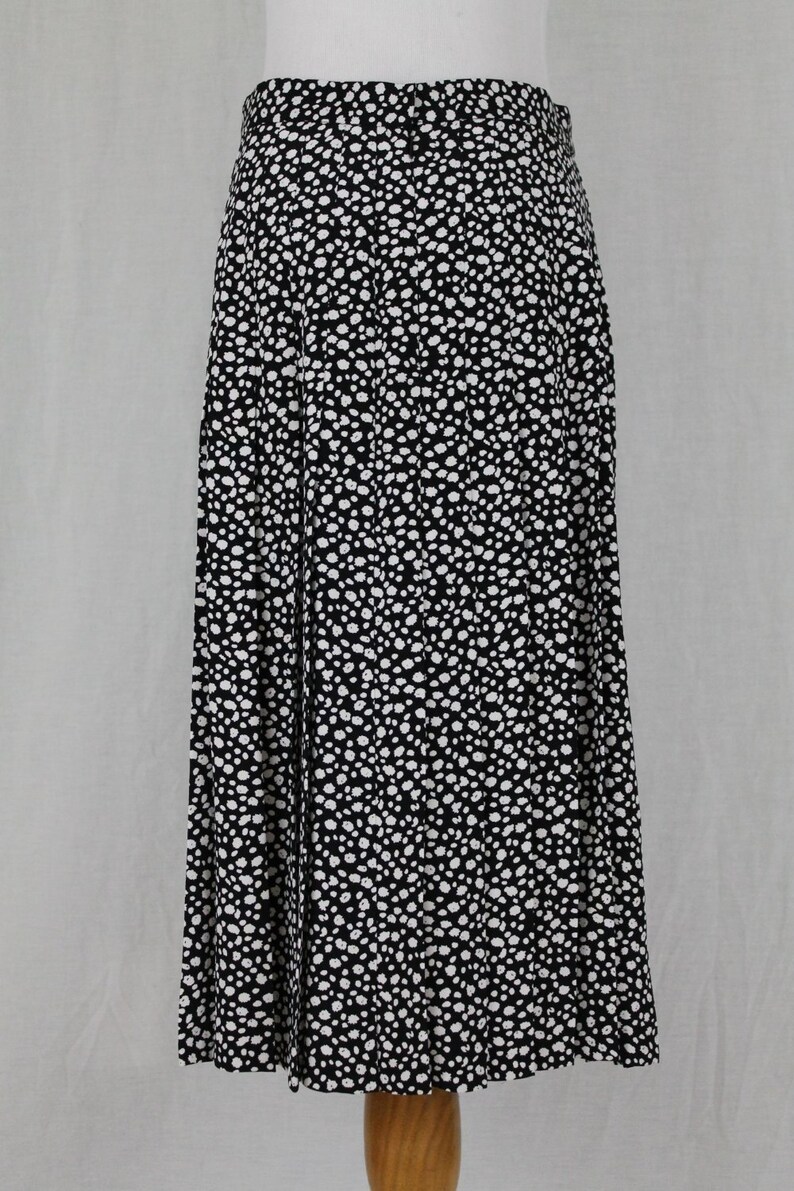 May include: A black and white pleated skirt with a polka dot pattern. The skirt is knee-length and has a fitted waist.