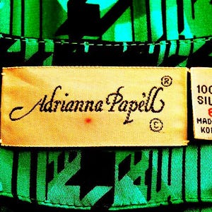May include: A close-up of a green and black patterned fabric with a label that reads "Adrianna Papell" and "100% Silk Made in Korea".