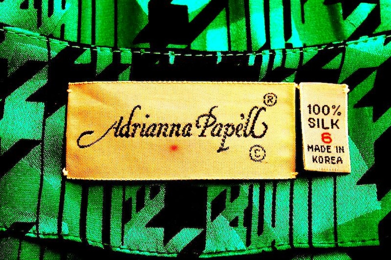May include: A close-up of a green and black patterned fabric with a label that reads "Adrianna Papell" and "100% Silk Made in Korea".