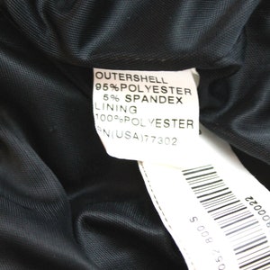 May include: A white tag with black text detailing the fabric composition of a black garment. The tag reads "OUTERSHELL 95% POLYESTER 5% SPANDEX LINING 100% POLYESTER RN(USA)77302". A barcode is visible on the bottom right corner of the tag.