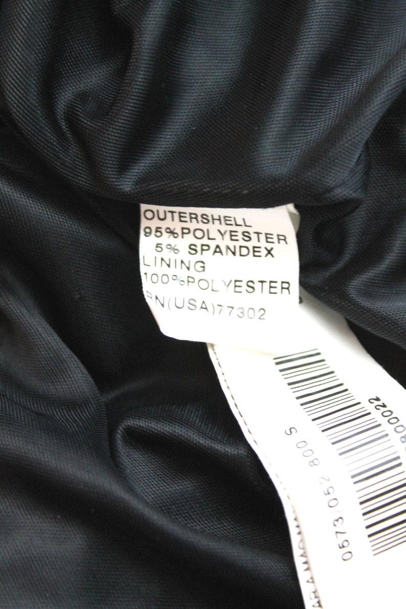 May include: A white tag with black text detailing the fabric composition of a black garment. The tag reads "OUTERSHELL 95% POLYESTER 5% SPANDEX LINING 100% POLYESTER RN(USA)77302". A barcode is visible on the bottom right corner of the tag.