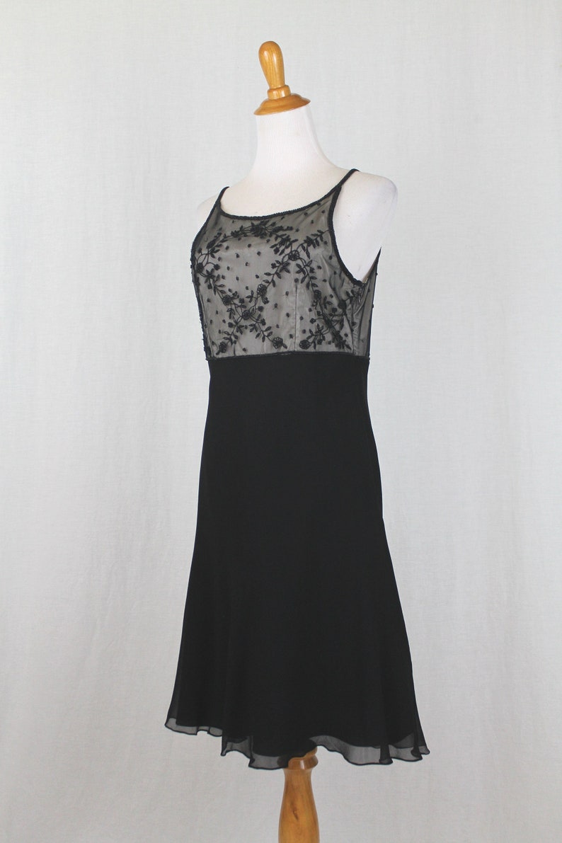 Pode incluir: Um vestido preto sem mangas com um corpete de renda transparente com um padr&atilde;o floral. A saia &eacute; de linha A e chega aos joelhos.