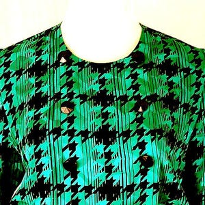 May include: A green and black houndstooth patterned blouse with a round neckline and button closures.