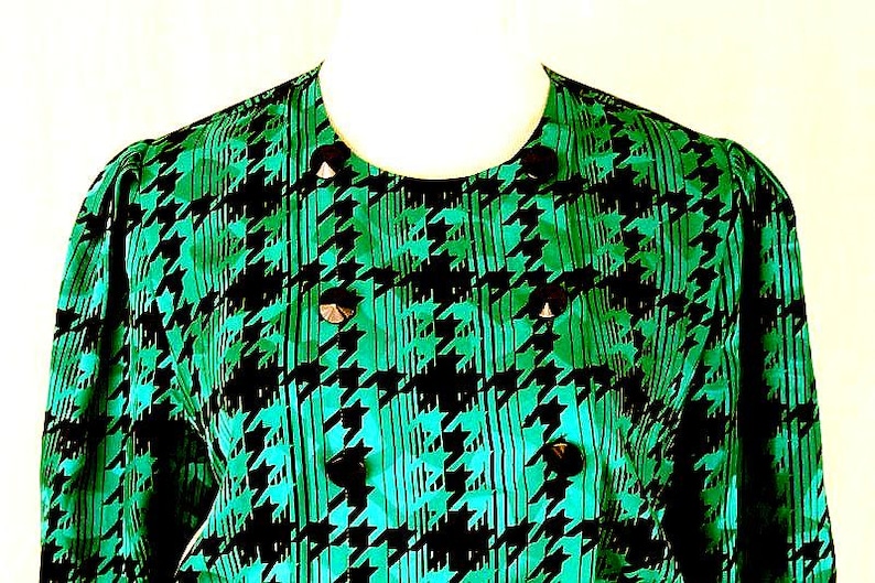 May include: A green and black houndstooth patterned blouse with a round neckline and button closures.