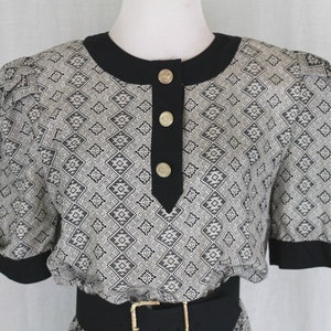 May include: A black and white patterned dress with a black collar and short sleeves. The dress has a black belt and gold buttons down the front.