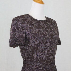 May include: A brown beaded top with a floral design. The top has short sleeves and a scalloped hem.