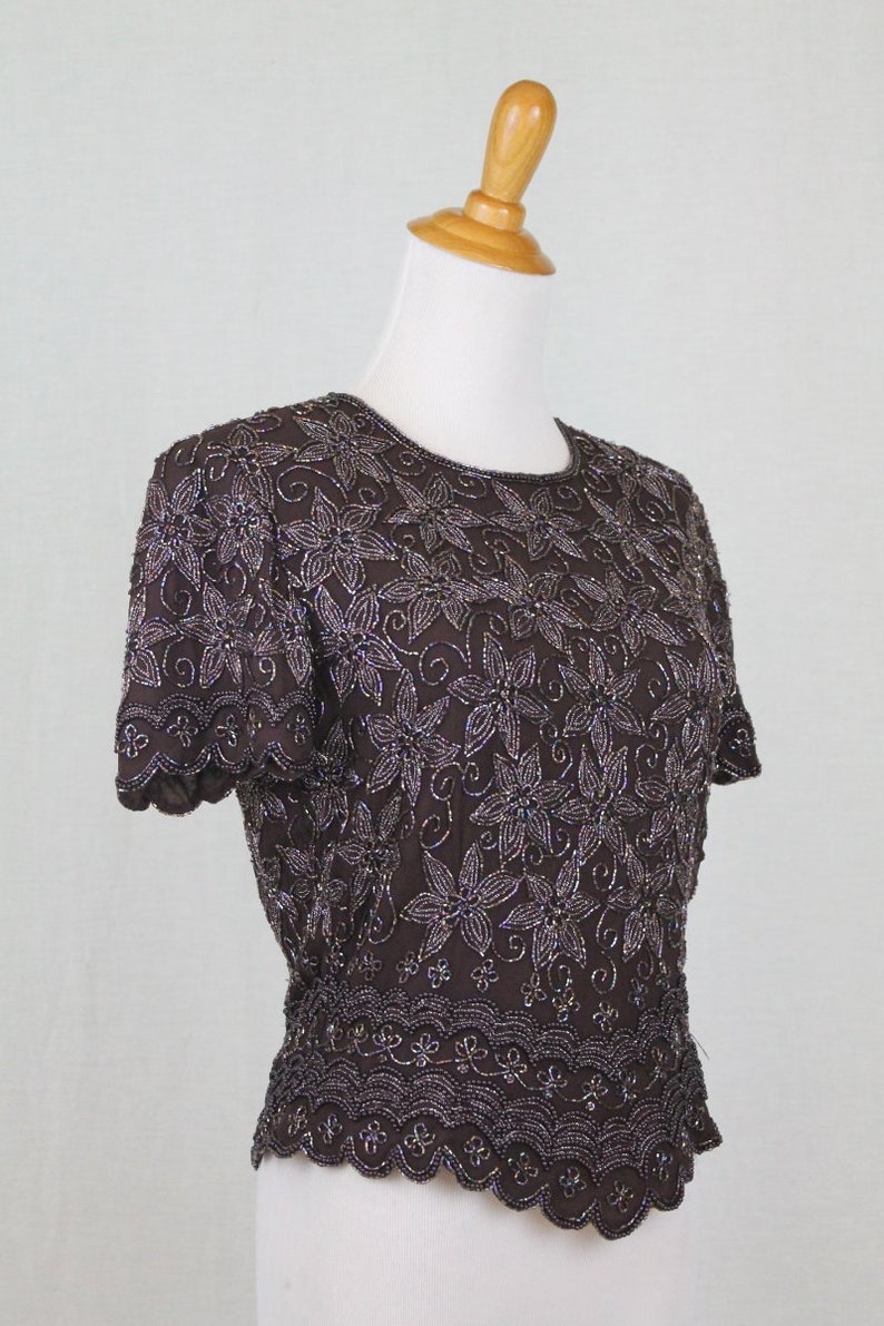 May include: A brown beaded top with a floral design. The top has short sleeves and a scalloped hem.