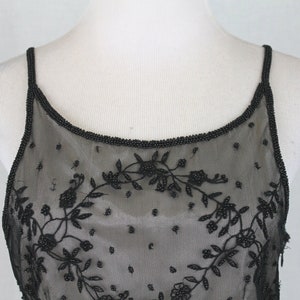 Pode incluir: Top preto com al&ccedil;as finas de espaguete com contas e design floral. O top &eacute; feito de tecido transparente e tem um decote redondo.
