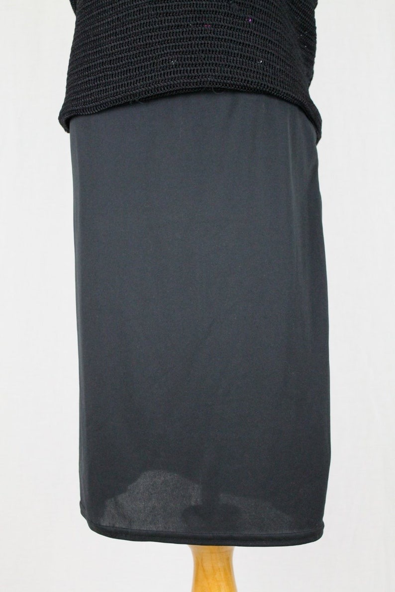May include: A black skirt made of a smooth, silky fabric. The skirt is knee-length and has a straight silhouette.