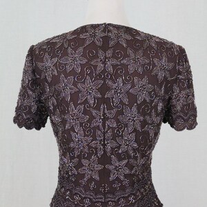 May include: A brown beaded top with a floral pattern. The top has short sleeves and a scalloped hem.