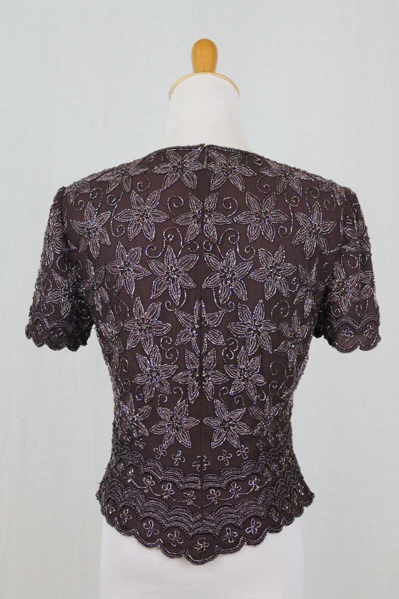 May include: A brown beaded top with a floral pattern. The top has short sleeves and a scalloped hem.