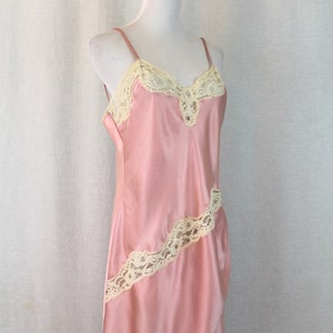 May include: A pink satin slip dress with delicate white lace trim. The dress has a V-neckline and adjustable straps.