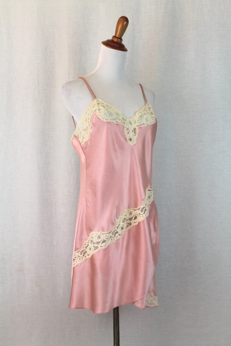 May include: A pink satin slip dress with delicate white lace trim. The dress has a V-neckline and adjustable straps.