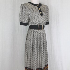 May include: A black and white patterned dress with a black belt and a colorful geometric trim at the hem. The dress has a fitted bodice and a pleated skirt.