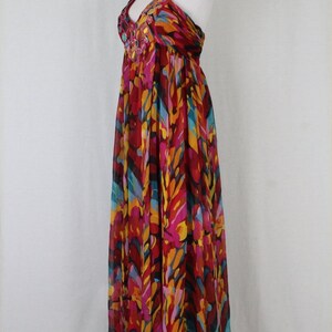 May include: A long, flowing halter dress with a colourful abstract print in shades of red, pink, yellow, blue, and black. The dress has a beaded neckline.