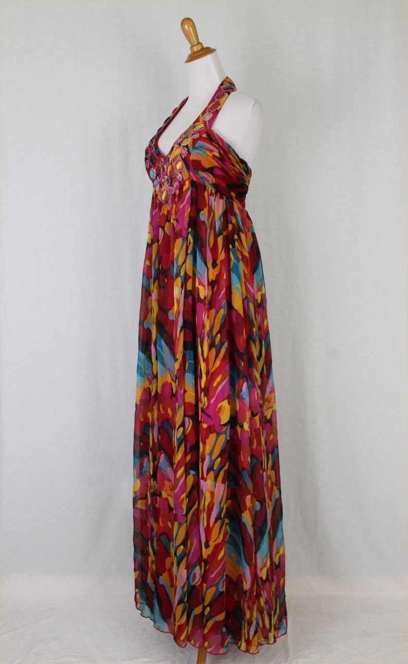 May include: A long, flowing halter dress with a colourful abstract print in shades of red, pink, yellow, blue, and black. The dress has a beaded neckline.