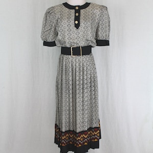 May include: A gray and black patterned dress with a black belt and a colorful geometric print at the hem. The dress has a round neckline and short sleeves.