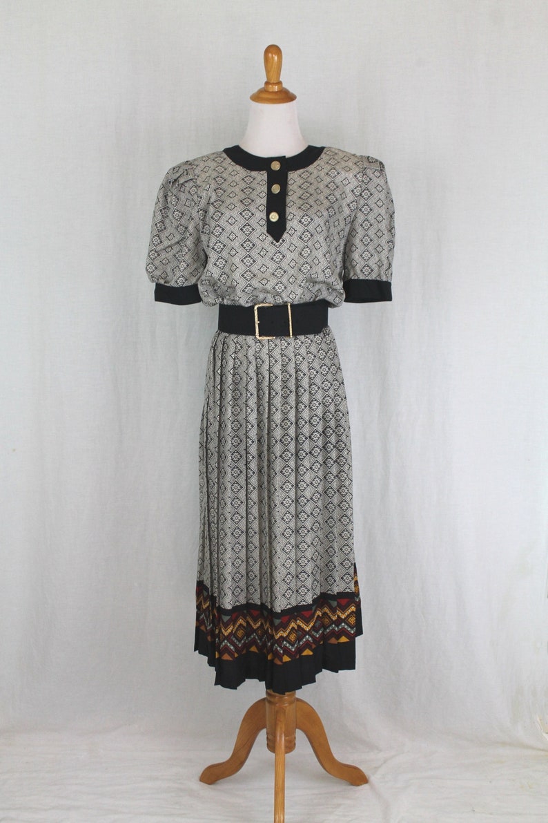 May include: A gray and black patterned dress with a black belt and a colorful geometric print at the hem. The dress has a round neckline and short sleeves.