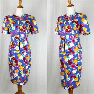 May include: A blue floral print skirt suit with a short-sleeved jacket and a fitted skirt. The suit has a white background with red, yellow, and pink flowers.