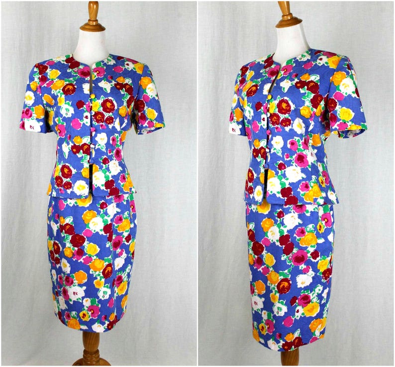 May include: A blue floral print skirt suit with a short-sleeved jacket and a fitted skirt. The suit has a white background with red, yellow, and pink flowers.
