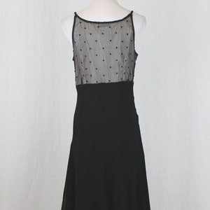 Pode incluir: Vestido preto sem mangas com um corpete de tule de bolinhas e uma saia preta lisa. A saia tem uma bainha festonada.