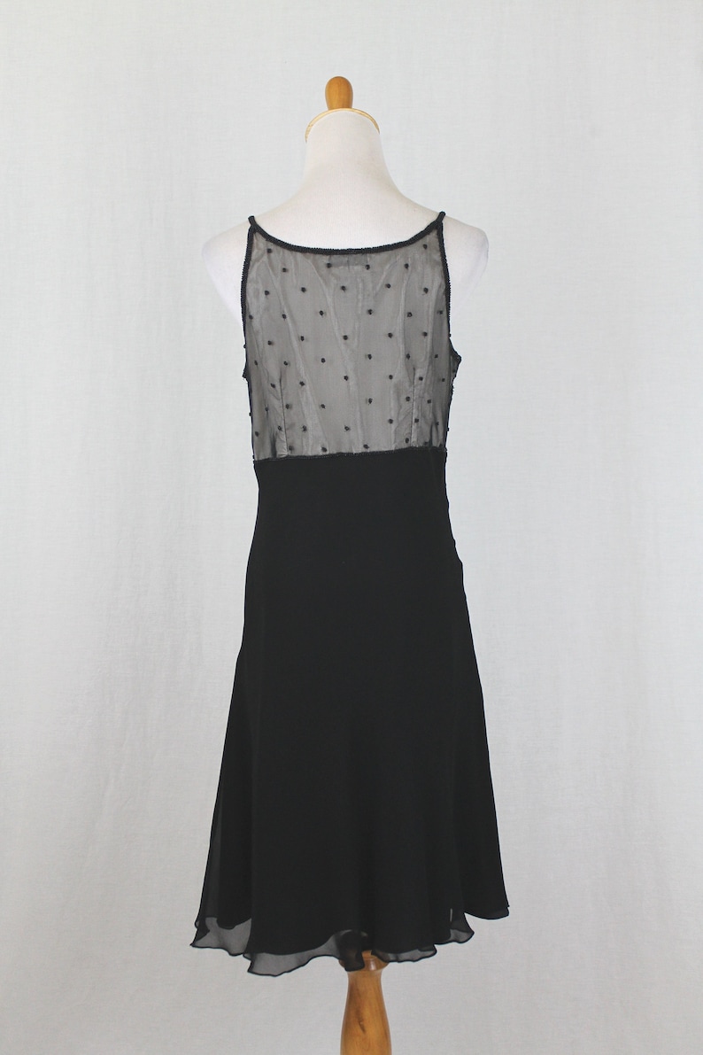 Pode incluir: Vestido preto sem mangas com um corpete de tule de bolinhas e uma saia preta lisa. A saia tem uma bainha festonada.