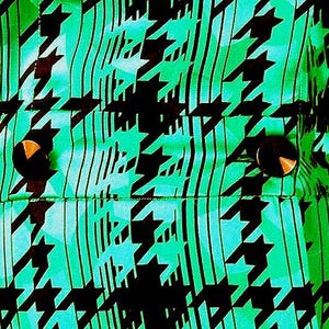 May include: A green and black patterned fabric with two black buttons. The fabric has a houndstooth pattern.
