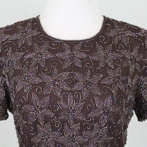May include: A brown beaded top with a floral design. The top has short sleeves and a round neckline.