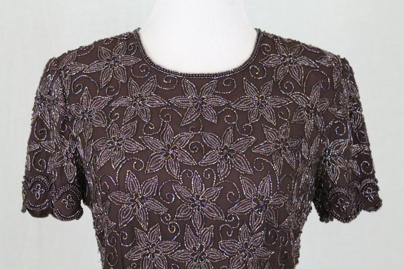 May include: A brown beaded top with a floral design. The top has short sleeves and a round neckline.