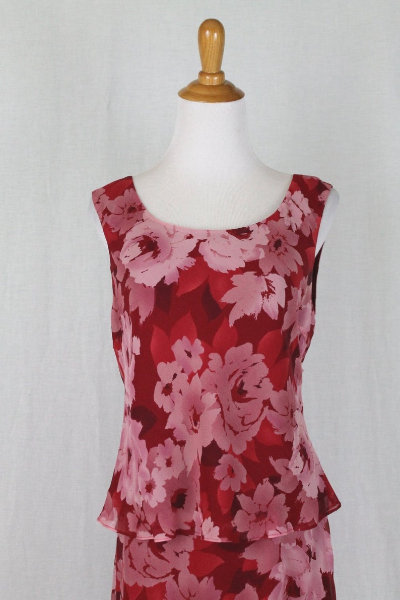 May include: A sleeveless dress with a red and pink floral print. The dress has a tiered skirt and a fitted bodice.