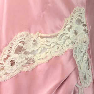 May include: A pink satin slip with a white lace trim. The lace trim is on the bottom edge of the slip and extends up the side.