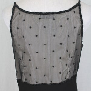 Pode incluir: Vestido preto sem mangas com um corpete transparente com contas e uma saia preta lisa.