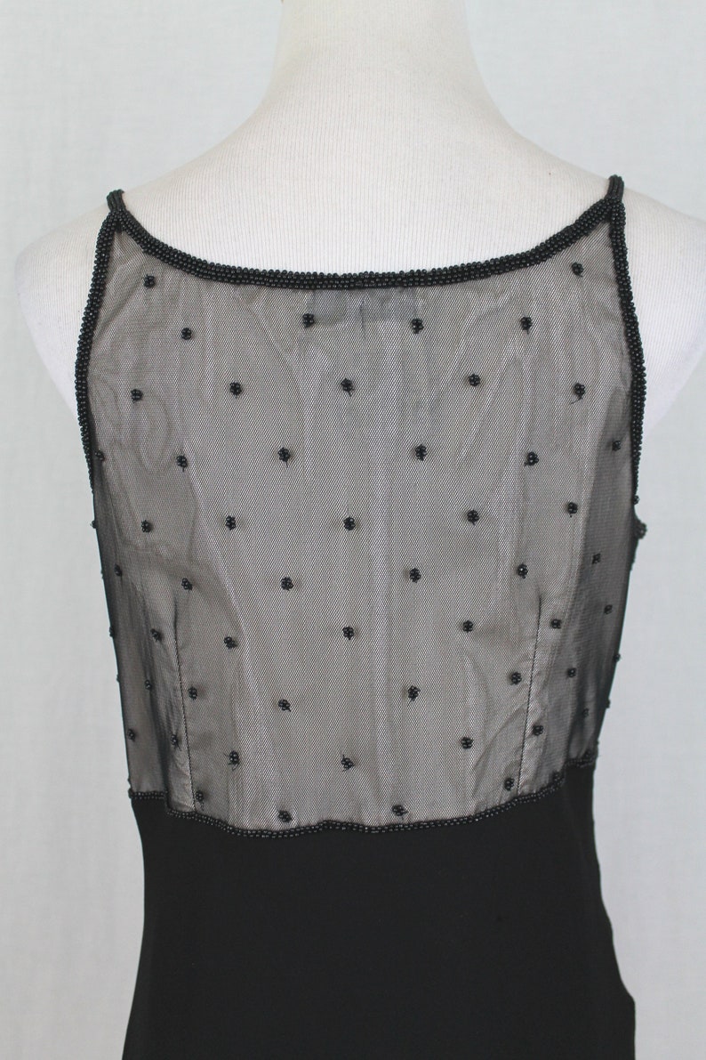 Pode incluir: Vestido preto sem mangas com um corpete transparente com contas e uma saia preta lisa.