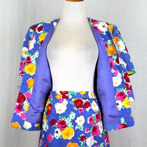 May include: A blue floral print skirt suit with a matching jacket. The jacket has a purple lining and the skirt has a blue background with pink, yellow, white, and red flowers.
