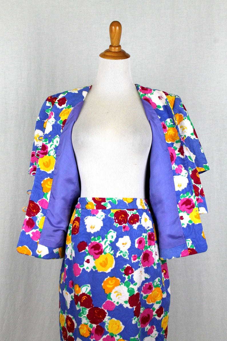 May include: A blue floral print skirt suit with a matching jacket. The jacket has a purple lining and the skirt has a blue background with pink, yellow, white, and red flowers.