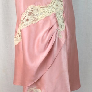 May include: A pink satin slip dress with white lace trim. The dress has a gathered detail on the front and a scalloped hem.