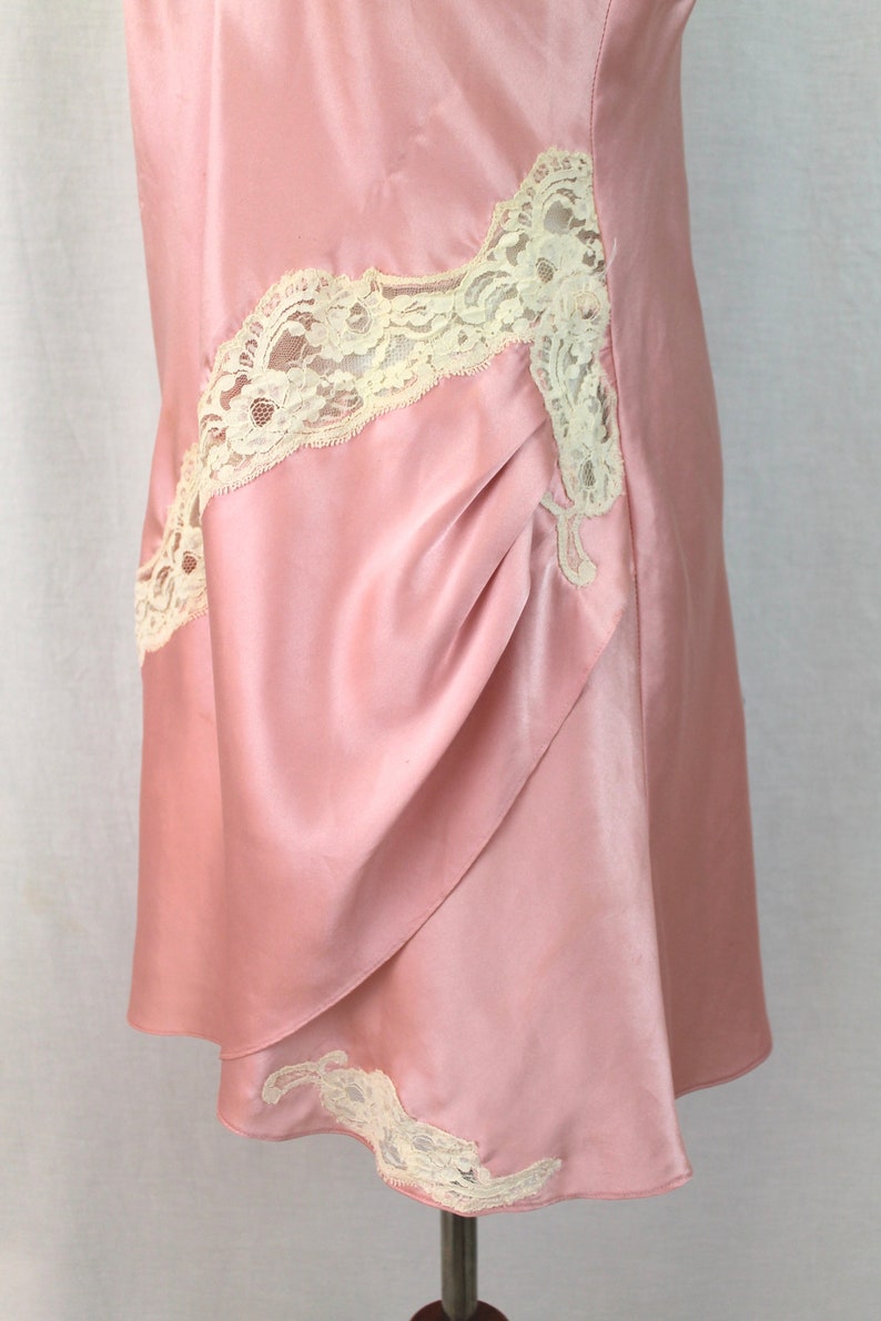 May include: A pink satin slip dress with white lace trim. The dress has a gathered detail on the front and a scalloped hem.
