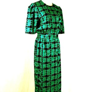 May include: A green and black houndstooth print dress with short sleeves and a button-up front. The dress is on a mannequin.