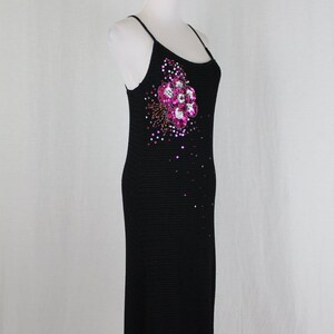 May include: A black sleeveless dress with a pink and silver flower embellishment on the front. The dress is made of a knit fabric and has a fitted silhouette.