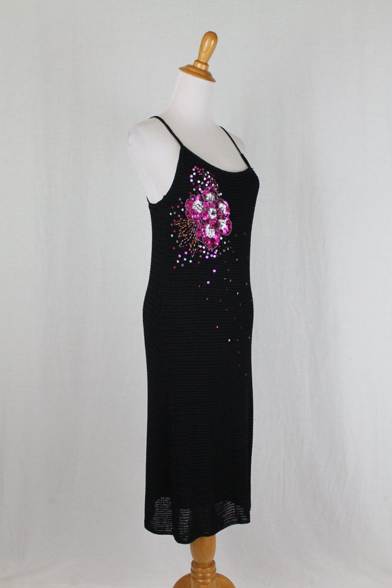 May include: A black sleeveless dress with a pink and silver flower embellishment on the front. The dress is made of a knit fabric and has a fitted silhouette.