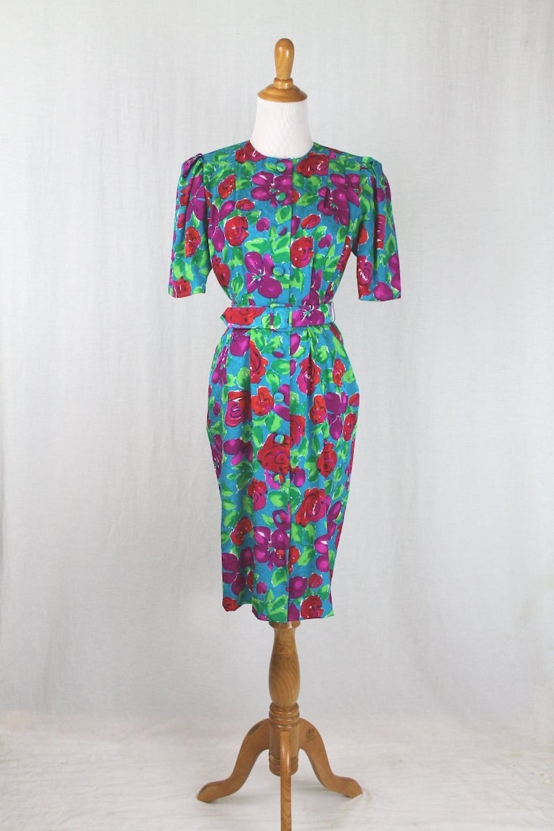 Puede incluir: Un vestido azul con estampado floral con flores rojas y moradas. El vestido tiene un frente abotonado y un cintur&oacute;n.