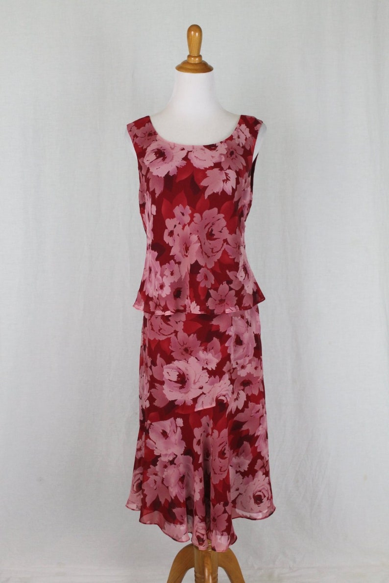 May include: A sleeveless, red and pink floral print dress with a tiered skirt. The dress has a scoop neck and a fitted bodice.