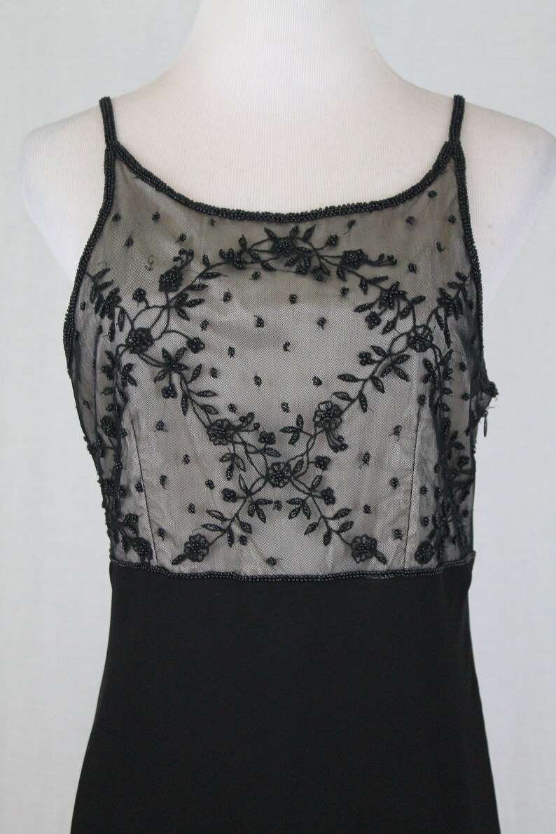 Pode incluir: Um vestido preto sem mangas com um corpete transparente de contas com um design floral. O corpete &eacute; forrado com um tecido preto.
