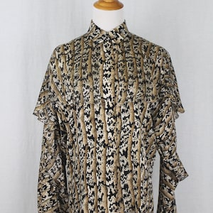 Puede incluir: Una blusa de manga larga con estampado marrón y negro, con cuello y puños con volantes. La blusa tiene cierre de botones en la parte delantera y un ajuste holgado.